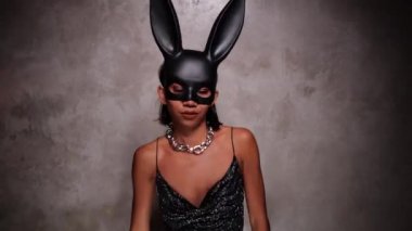 Siyah elbiseli ve tavşan maskeli güzel Asyalı kadının portresi spot ışıklarında neşe içinde dans ediyor.