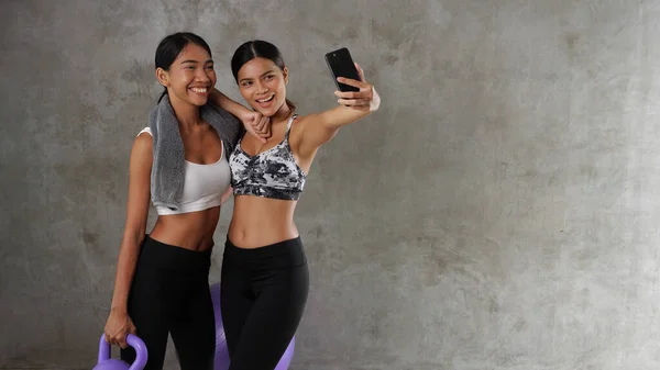 两名漂亮的年轻亚洲女子在体育馆用智能手机自拍 快乐的女性朋友在体育中心度过了他们的闲暇时光 — 图库照片