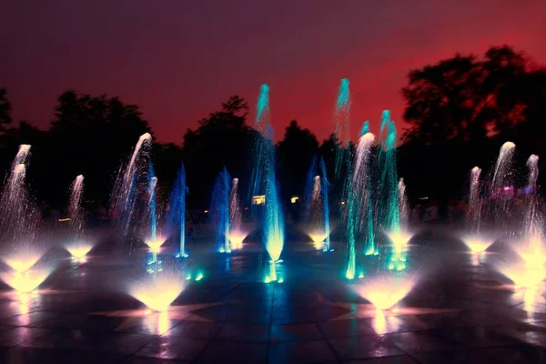 Wielokolorowe fontanny miejskie na tle nieba zachód słońca. — Zdjęcie stockowe