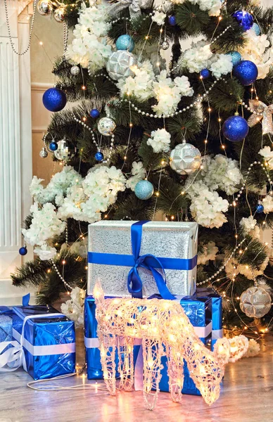 Julklappar och glödande julrådjur nära julgran — Stockfoto