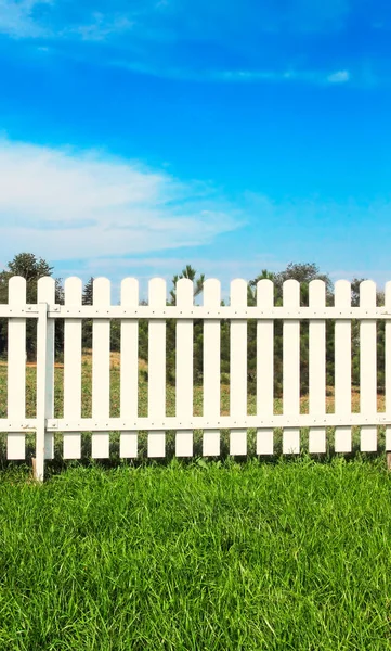 Weißer Holzzaun auf grünem Gras vor blauem Himmel. — Stockfoto