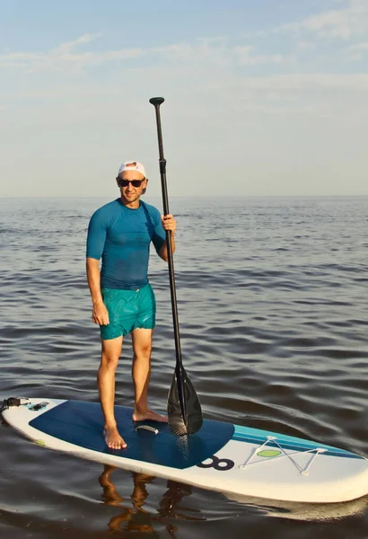 SAP Board surfing. Man is training on a SUP board in the summer sea at sunny day.