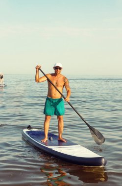 Gençler yaz denizinde bir SUP tahtasında eğitim görüyor. SAP yönetim kurulu sörfü. 