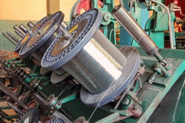 Esnek metal hortum üretim hattı. Örgü makinesinin çelik tel makaraları yakın plan..