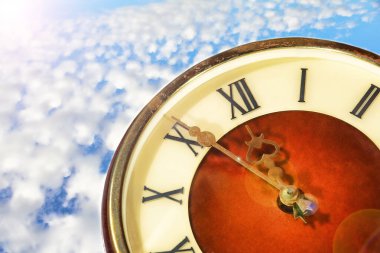 Bulutlu gökyüzü arkaplanındaki klasik saat yüzü yakınlaştırıldı.