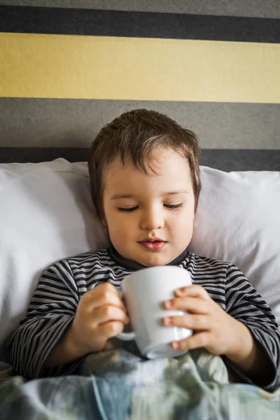 침대에 누워의 약의 컵을 보고 건강에 해로운 소년 — 스톡 사진