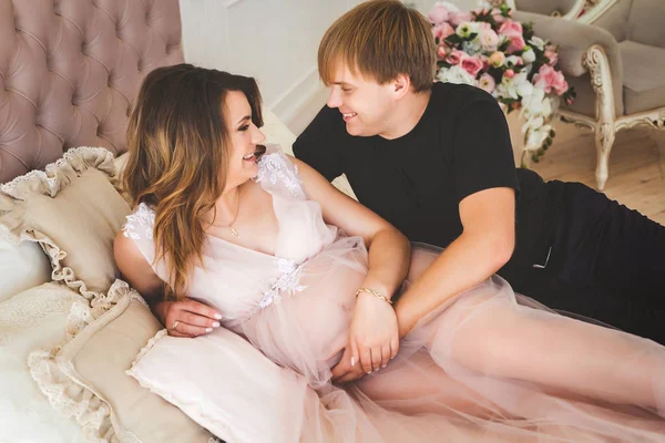 Молода щаслива вагітна жінка лежить на затишному ліжку з красивим чоловіком — стокове фото