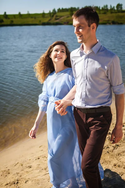 Facet i kobieta w ciąży, chodzenie na brzegu razem trzymając się za ręce — Zdjęcie stockowe