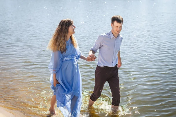 Future parents walking on water along river shore holding hands together — Stock Photo, Image