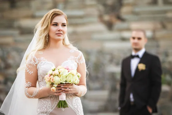 Невеста хранит прекрасный свадебный букет и жениха, стоящих позади — стоковое фото