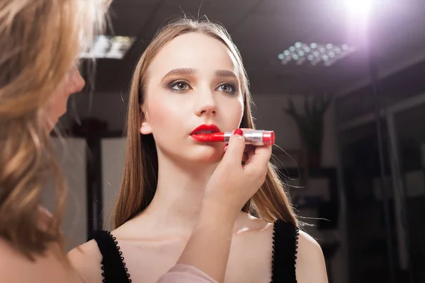 Mulher maquiagem aplicando brilho labial vermelho em um modelo — Fotografia de Stock