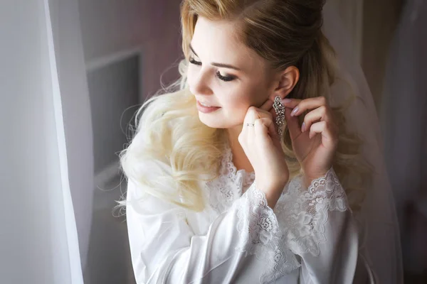 Bride in white dressing gown wearing earrings — Stock Photo, Image