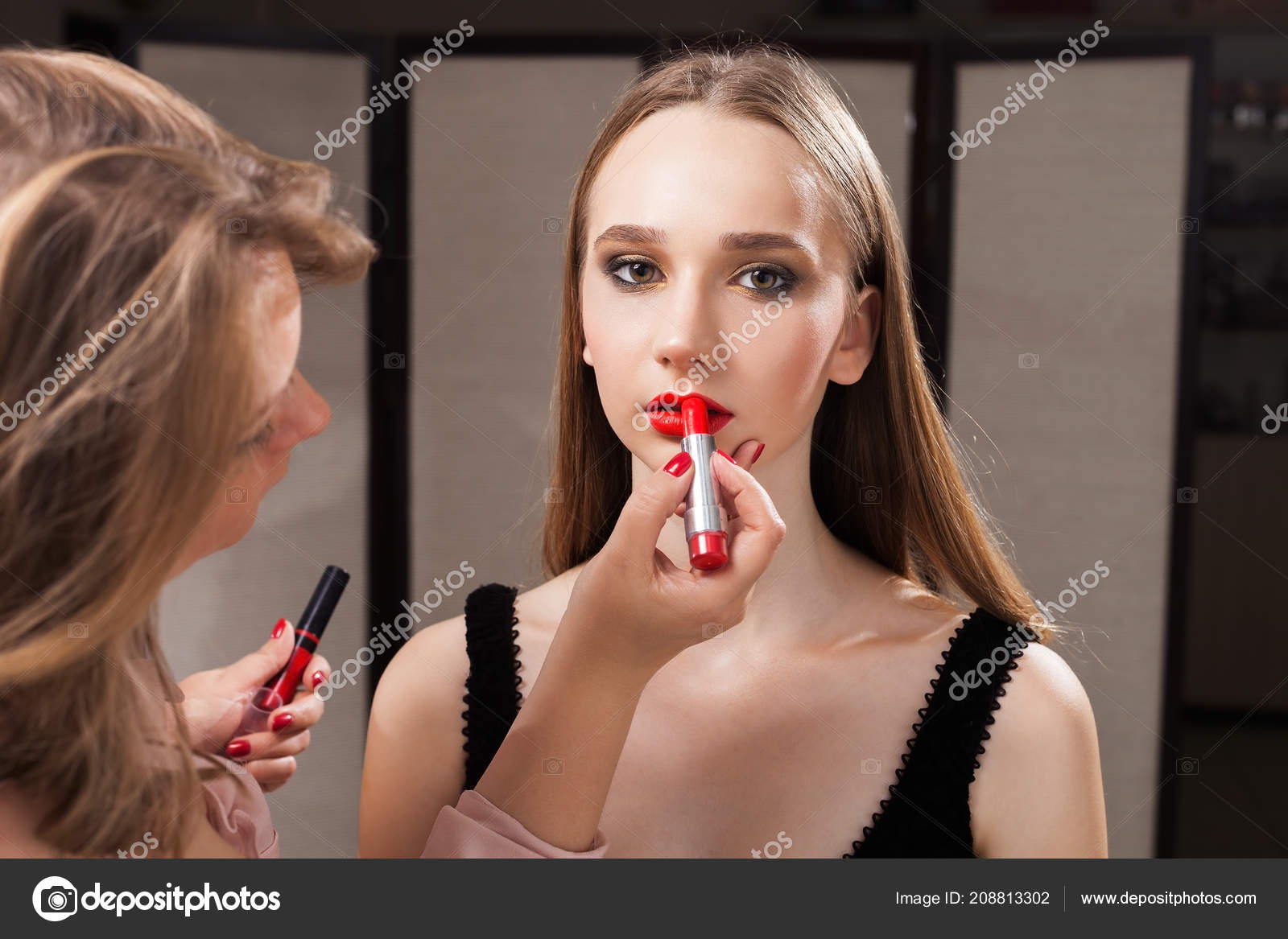 Makeup woman applying red lipstick on a model Stock Photo by ©luckyphoto 208813302