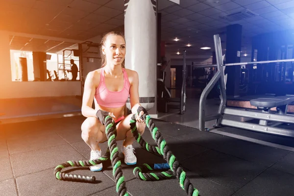 Chica delgada haciendo ejercicios con un cable en el gimnasio — Foto de Stock