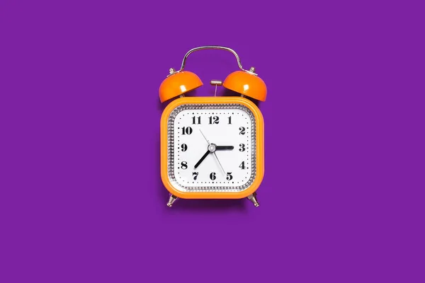 Оранжевый будильник на фиолетовом фоне — стоковое фото