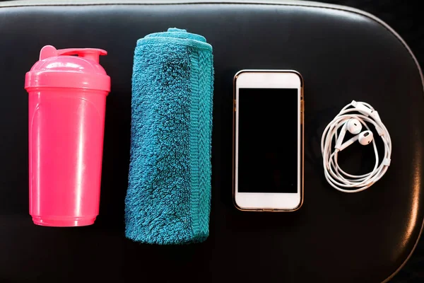 Telefone inteligente, fones de ouvido, toalha e uma coqueteleira em um banco em um ginásio — Fotografia de Stock