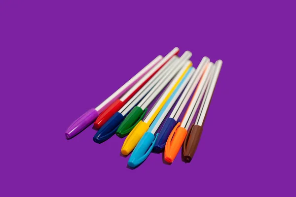 Colored pens lying on a purple background — Stock Photo, Image