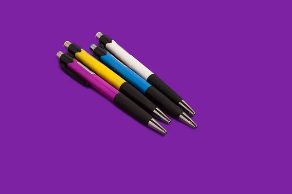 Fyra färgade pennor liggandes på en lila bakgrund — Stockfoto