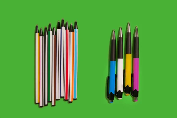 Två rad av färgade pennor liggandes på en grön bakgrund — Stockfoto