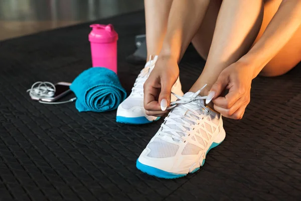 Mujer atando cordones de zapatillas en el gimnasio —  Fotos de Stock