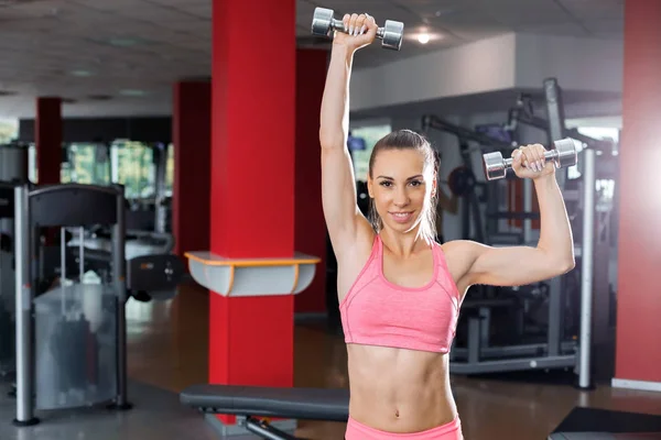 Atlética joven sonriente mujer levantando pesas en el gimnasio —  Fotos de Stock