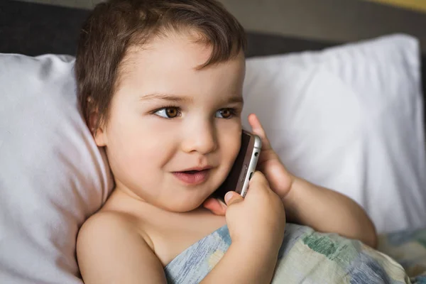 Маленький хлопчик говорить мобільний телефон лежить на ліжку вранці — стокове фото