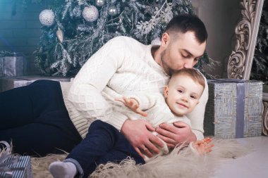 sarılma ve öpüşme gülümseyen bebek evlat Noel ağacı yakınındaki halı döşeme mutlu yakışıklı babası