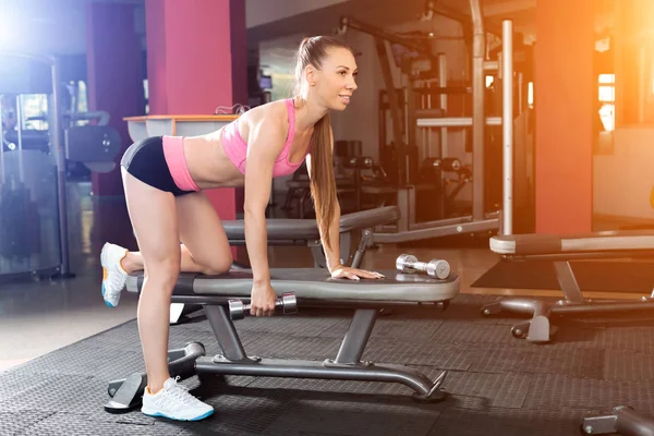 Chica atlética haciendo ejercicio con pesas en el banco — Foto de Stock