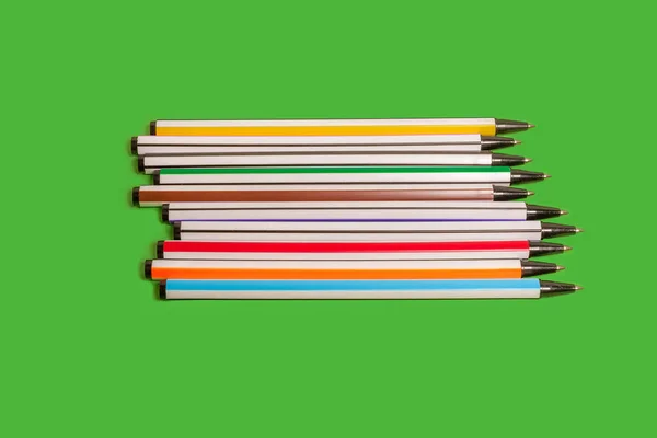 Uppsättning färgade pennor liggande på en grön bakgrund — Stockfoto