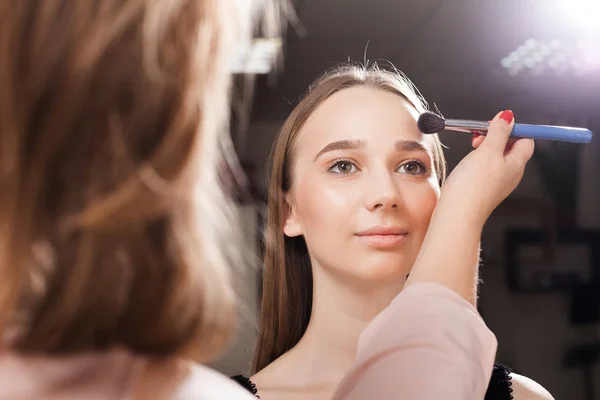Artista de maquiagem aplicando um pó em uma testa de uma menina — Fotografia de Stock