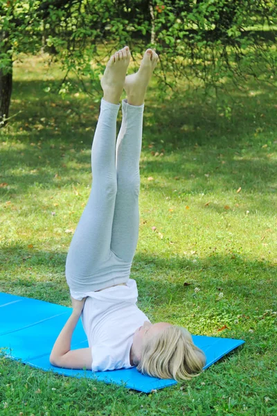 Güzel sarışın varoluş kız ışık giyim pratik yoga mat parkta. Sağlıklı bir yaşam tarzı. Açık havada egzersiz. 