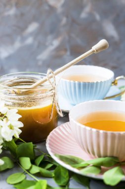 Vintage bardak çay yanında bir kavanoz bal ve akasya gri bir tablo. Doğal tatlandırıcı ballı çayı