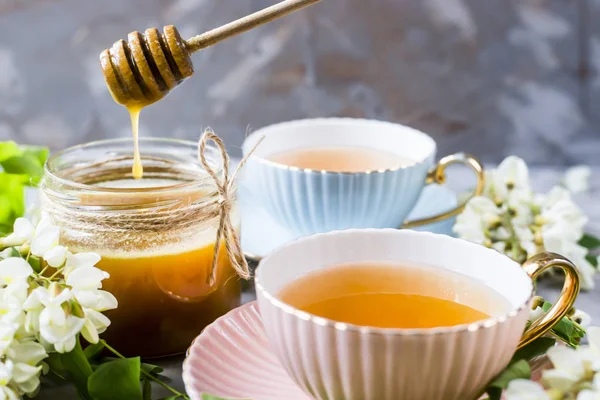 蜂蜜とアカシア グレー テーブルの上の瓶の横に紅茶とビンテージ カップ 天然甘味料蜂蜜とお茶 — ストック写真