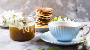 Börek yanında bir fincan çay ve bir kavanoz bal akasya çiçekleri arasında gri bir arka plan üzerine yığını. Bahar lezzetli breakfast