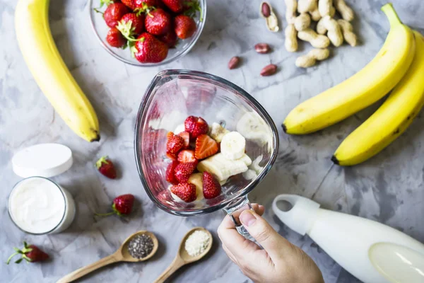 Çilek Muz smoothies blendet bir cam kase yanındaki gri bir tablo yapmak için malzemeler. Sağlıklı kahvaltı kavramı yemek. Üstten görünüm, düz yatıyordu