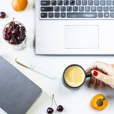 Çalışma alanı laptop ve defter meyveler ve meyve snack ve bir fincan kahve bir kadın elinde beyaz bir tablo ile. Üstten görünüm, düz yatıyordu