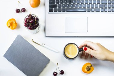 Çalışma alanı laptop ve defter meyveler ve meyve snack ve bir fincan kahve bir kadın elinde beyaz bir tablo ile. Üstten görünüm, düz yatıyordu