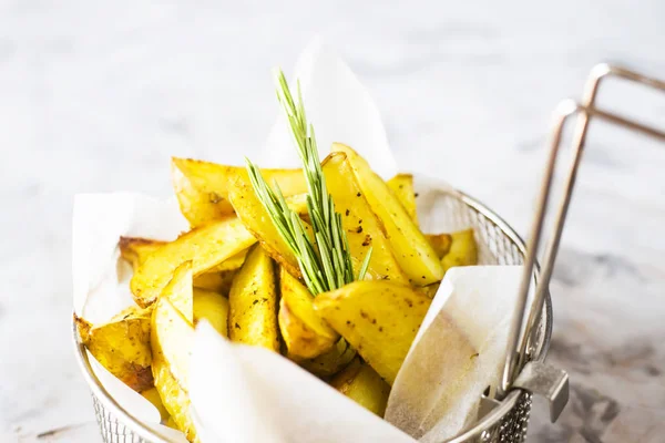 Sliced baked potatoes with spices and rosemary in a grid for deep frying. Fresh vegetable dish appetizer