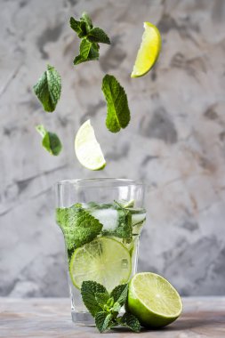 Nane ve limon yaprakları ile mojito buzlu cam içine gri bir arka plan üzerinde uçmak. Sihirli öğeleri uçan havaya yükselme. Yaz içeceği