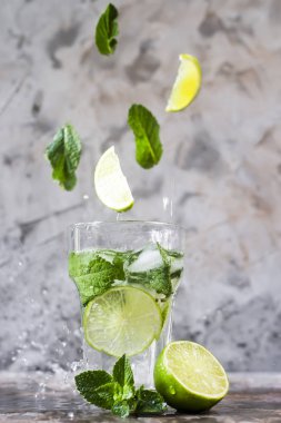 Nane ve limon yaprakları ile mojito buzlu cam içine gri bir arka plan üzerinde uçmak. Sihirli öğeleri uçan havaya yükselme. Yaz içeceği. Su sprey ile