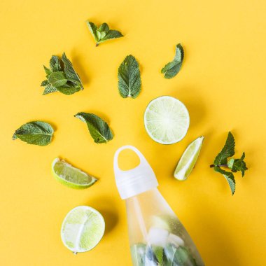 Mojito kireç ve ferahlatıcı bir yaz içeceği şeffaf bir şişeyle yanında sarı bir arka plan üzerine nane için malzemeler. Üstten görünüm, düz yatıyordu