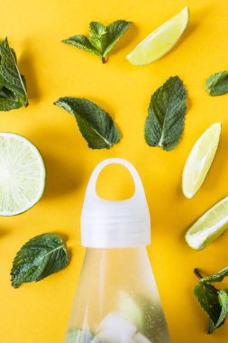 Mojito kireç ve ferahlatıcı bir yaz içeceği şeffaf bir şişeyle yanında sarı bir arka plan üzerine nane için malzemeler. Üstten görünüm, düz yatıyordu