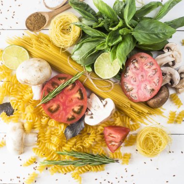 Pişirme - yemek makarna, fesleğen, sebze, kireç ve baharat beyaz ahşap bir masa bir yığın üzerinde. Üstten görünüm, düz yatıyordu