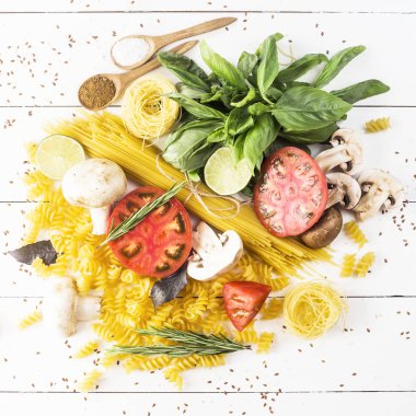 Pişirme - yemek makarna, fesleğen, sebze, kireç ve baharat beyaz ahşap bir masa bir yığın üzerinde. Üstten görünüm, düz yatıyordu