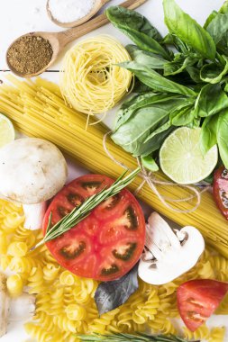 Pişirme - yemek makarna, fesleğen, sebze, kireç ve baharat beyaz ahşap bir masa bir yığın üzerinde. Üstten görünüm, düz yatıyordu
