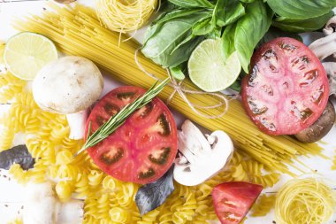 Pişirme - yemek makarna, fesleğen, sebze, kireç ve baharat beyaz ahşap bir masa bir yığın üzerinde. Üstten görünüm, düz yatıyordu