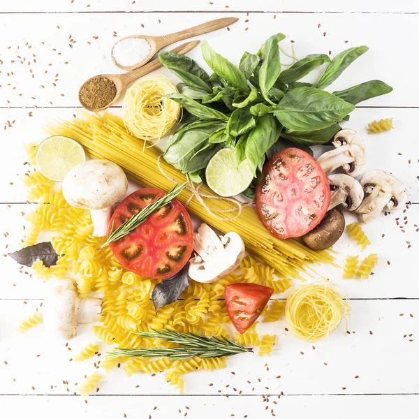 Pişirme - yemek makarna, fesleğen, sebze, kireç ve baharat beyaz ahşap bir masa bir yığın üzerinde. Üstten görünüm, düz yatıyordu