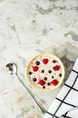 Bir tabak yulaf ezmesi ile ahududu ve yaban mersini beyaz kareli peçete yanındaki gri bir tablo. Sağlıklı yaz kahvaltı. Üstten görünüm, düz yatıyordu, boşaltmak