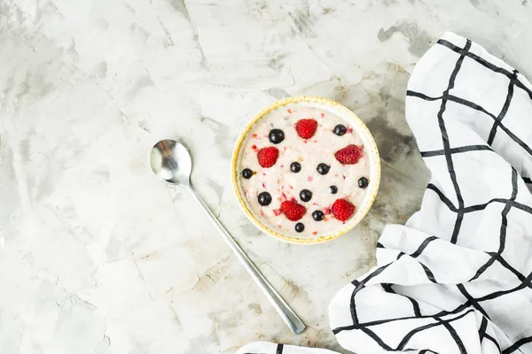 Bir tabak yulaf ezmesi ile ahududu ve yaban mersini beyaz kareli peçete yanındaki gri bir tablo. Sağlıklı yaz kahvaltı. Üstten görünüm, düz yatıyordu, boşaltmak