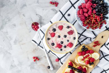 Bir tablo ile sağlıklı bir yaz kahvaltı - yulaf ezmesi çilek, kuş üzümü ve ahududu ve fıstık ezmesi, muz ve çeşitli meyveler ile bir sandviç. Üstten görünüm, düz yatıyordu